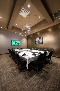 Private and elegant meeting room with a U-shaped table covered with a white tablecloth, black chairs, modern pendant lighting, and a themed painting on the gold wall.