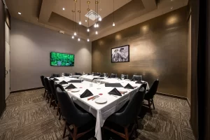 View of the event room set up with a U-shaped table, white tablecloths, folded black napkins, and decorative ceiling lighting, in a sophisticated setting.