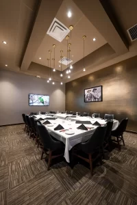 Conference space with a U-shaped table, black upholstered chairs, elegantly set table, wall with gold texture, and soft ambient lighting.