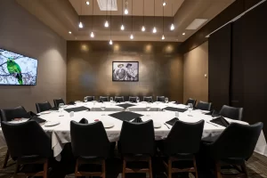 Private dining room for meetings, highlighting the central table, black leather chairs, gold wall with framed art, and ceiling chandelier with pendant lights.