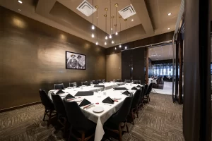 Space for corporate events with a U-shaped table arrangement, a gold accent wall with a painting, a view of an outdoor corridor, and elegant lighting.