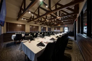 Perspective view of a spacious banquet room with dark wood-paneled walls, wooden blinds, and a long formal table arrangement, perfect for large group meetings or dining events.