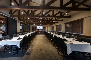 A view of a long banquet table set for a professional event, highlighting the clean white linens, black napkins, and the rustic charm of the exposed wooden ceiling structure.