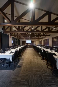 Interior of a meeting and dining space showcasing a long, symmetrical table arrangement under high wooden vaulted ceilings, creating a professional and inviting atmosphere.
