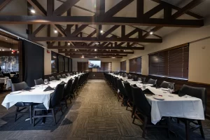Perspective view of a large meeting room featuring vaulted ceilings, wooden trusses, and long rows of tables with white tablecloths and black chairs, set for a conference or dinner.