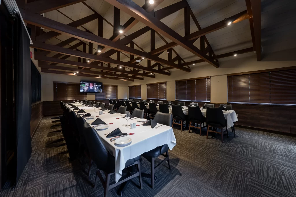 Side-angle view of a formal banquet room with a long table layout, emphasizing the architectural details of the wooden vaulted ceiling and professional table settings.