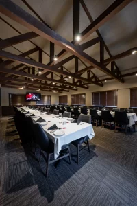 Interior of an event space featuring a long U-shaped table arrangement, soft ambient lighting, and a view into an adjacent area, highlighting the professional and welcoming atmosphere.