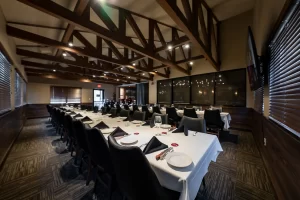 A formal event space featuring rows of neatly arranged tables, a high wooden-beamed ceiling, and a clean, professional aesthetic suitable for conferences or private parties.