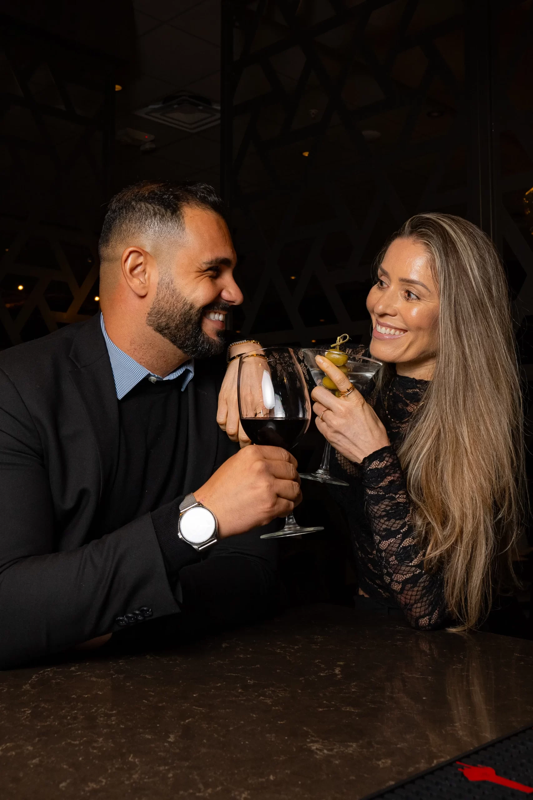 A smiling couple toasting drinks in a dimly lit restaurant.