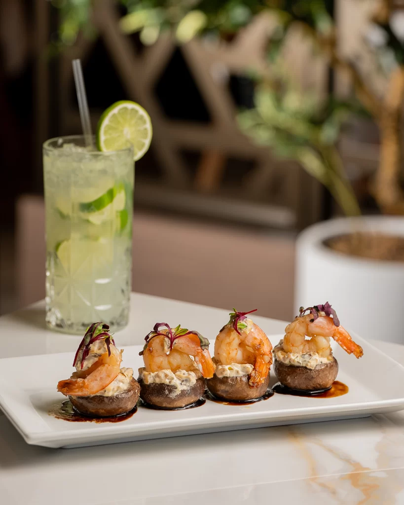 Gourmet shrimp appetizer presentation paired with a citrus cocktail in a refined dining setting