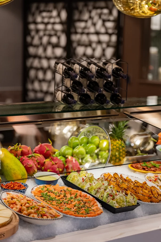 Upscale buffet display with fresh fruits, seafood appetizers, and curated plating under warm ambient lighting