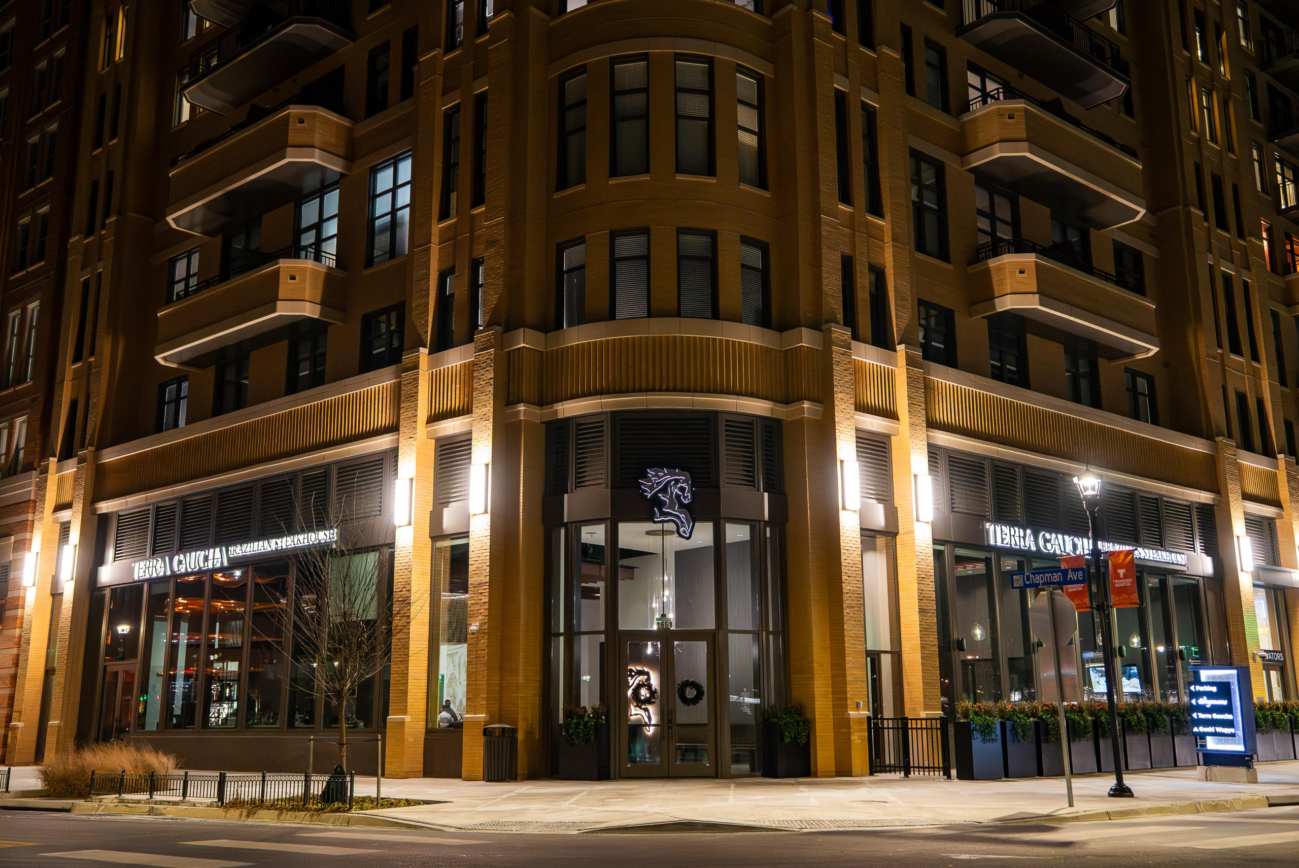 Terra Gaucha restaurant exterior at night, featuring a modern corner building with warm architectural lighting, large glass windows, and an upscale urban presence